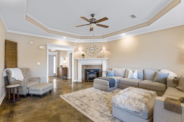 living room featuring a tiled fireplace, a tray ceiling, ornamental molding, and ceiling fan