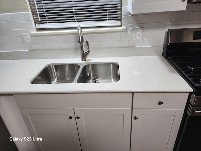 details with stainless steel range oven, sink, white cabinets, and backsplash