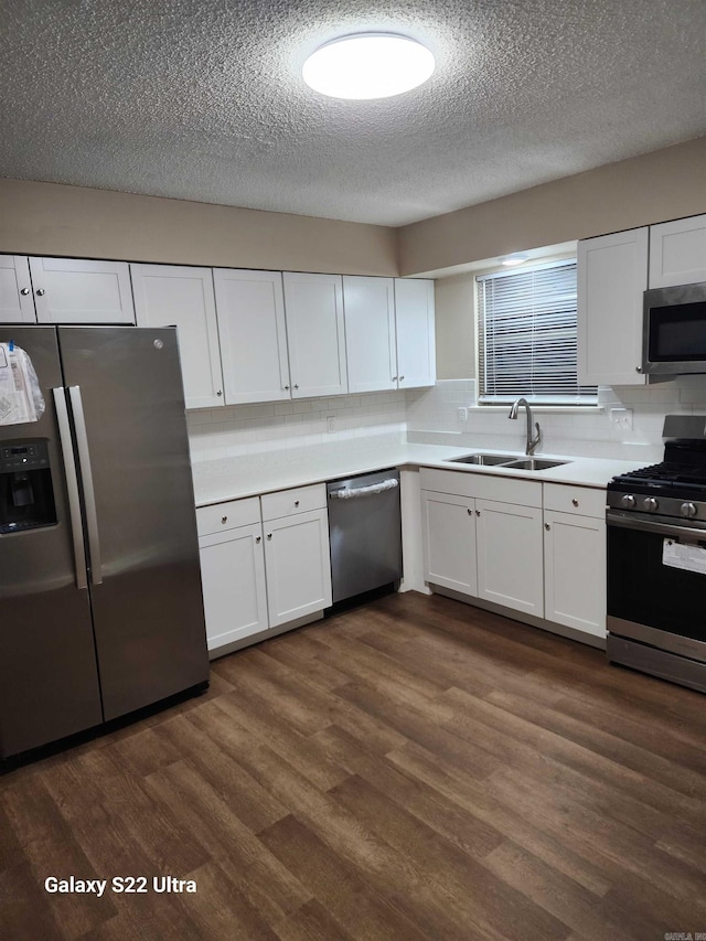 kitchen featuring dark wood-type flooring, sink, appliances with stainless steel finishes, white cabinets, and backsplash