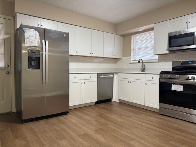 kitchen featuring sink, light hardwood / wood-style flooring, white cabinetry, stainless steel appliances, and decorative backsplash