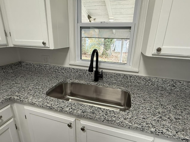 room details featuring white cabinetry, sink, and light stone counters