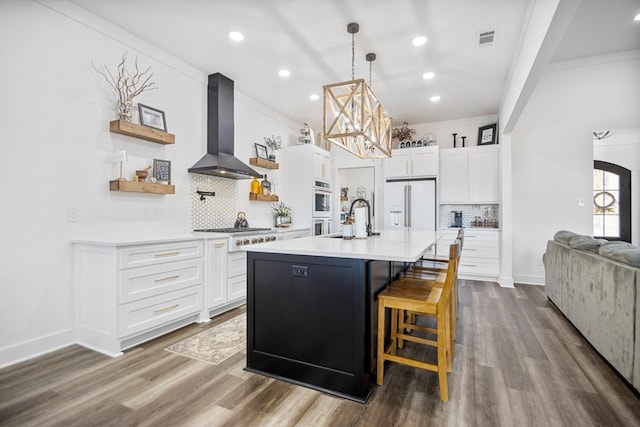 kitchen featuring white cabinetry, a kitchen island with sink, wall chimney range hood, and paneled refrigerator