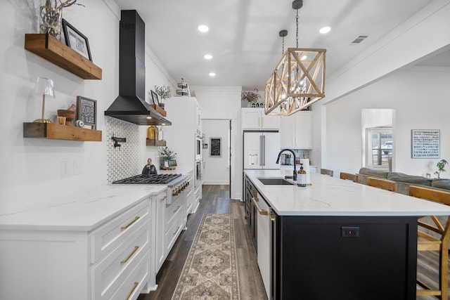 kitchen featuring sink, white cabinetry, a kitchen bar, decorative light fixtures, and wall chimney exhaust hood