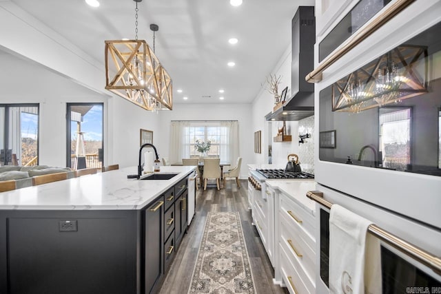 kitchen with pendant lighting, sink, an island with sink, white cabinets, and wall chimney exhaust hood