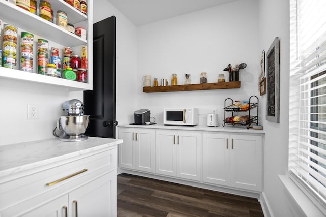 bar featuring dark hardwood / wood-style flooring, a healthy amount of sunlight, white cabinets, and light stone counters