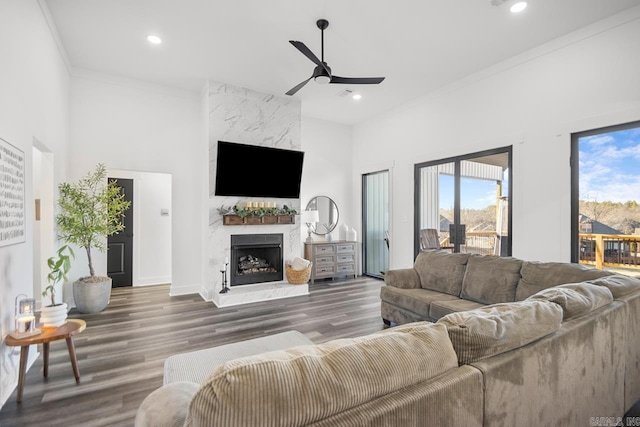 living room with ornamental molding, hardwood / wood-style flooring, ceiling fan, a premium fireplace, and a high ceiling