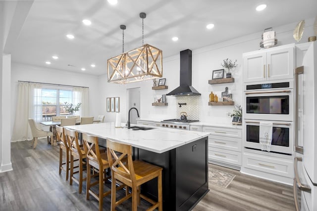 kitchen with white cabinetry, sink, a kitchen island with sink, white appliances, and wall chimney exhaust hood