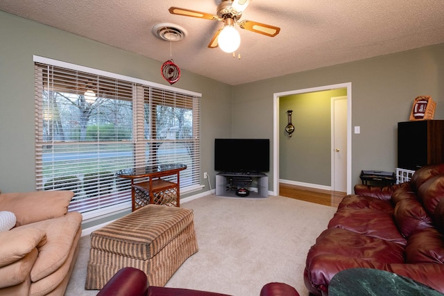 living room with ceiling fan, light carpet, and a textured ceiling