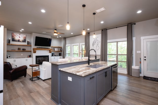 kitchen with sink, decorative light fixtures, a center island with sink, gray cabinets, and light stone countertops