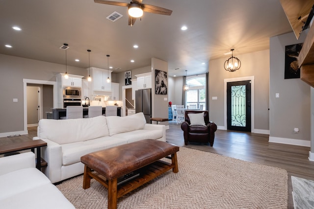 living room with ceiling fan with notable chandelier, sink, and light wood-type flooring