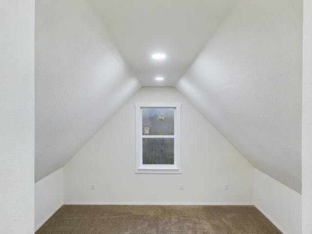 additional living space featuring lofted ceiling and dark colored carpet