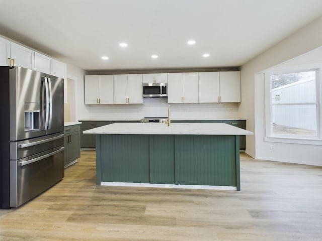 kitchen with white cabinetry, stainless steel appliances, light stone countertops, a center island with sink, and decorative backsplash