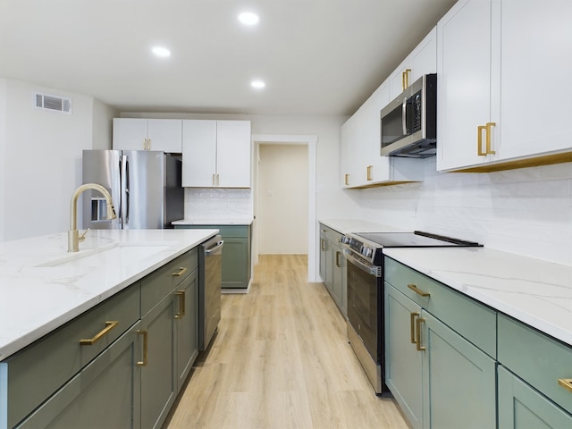 kitchen featuring sink, white cabinetry, light wood-type flooring, appliances with stainless steel finishes, and light stone countertops