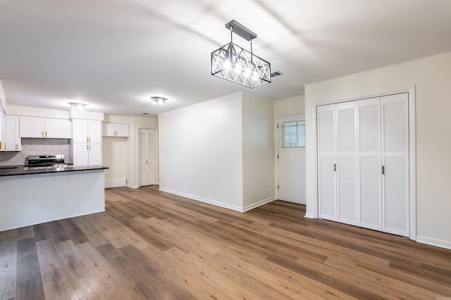 kitchen featuring hardwood / wood-style flooring, hanging light fixtures, tasteful backsplash, stainless steel range, and white cabinets