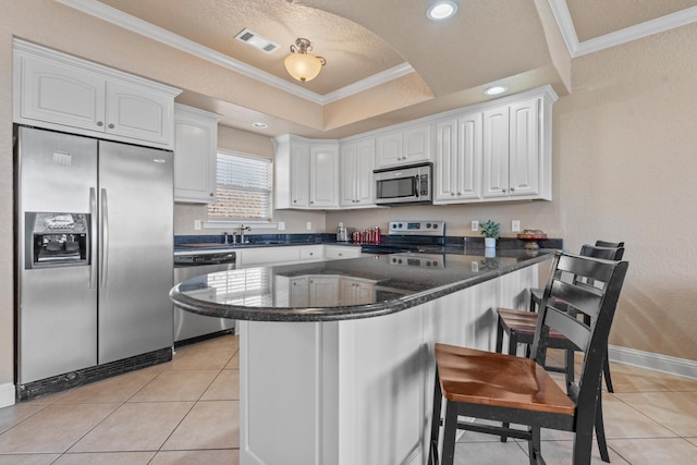 kitchen with stainless steel appliances, white cabinetry, crown molding, and a tray ceiling