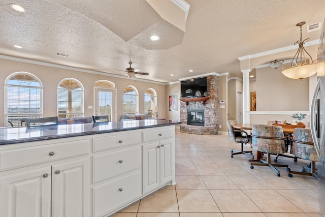 kitchen featuring pendant lighting, a stone fireplace, light tile patterned floors, and white cabinets