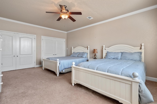 carpeted bedroom with ceiling fan, ornamental molding, and two closets