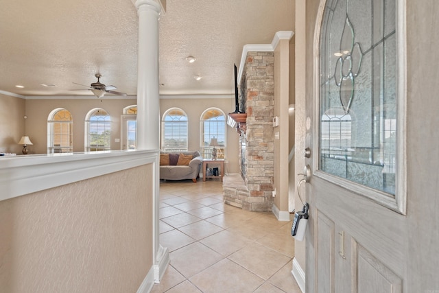 tiled foyer entrance with a textured ceiling, ornamental molding, ceiling fan, a fireplace, and decorative columns