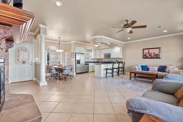 living room featuring light tile patterned floors, crown molding, ceiling fan, decorative columns, and a textured ceiling