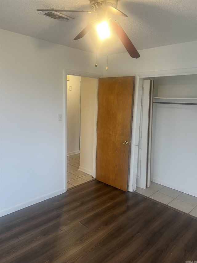 unfurnished bedroom with ceiling fan, dark wood-type flooring, a textured ceiling, and a closet