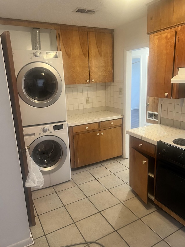 clothes washing area featuring stacked washing maching and dryer and light tile patterned floors