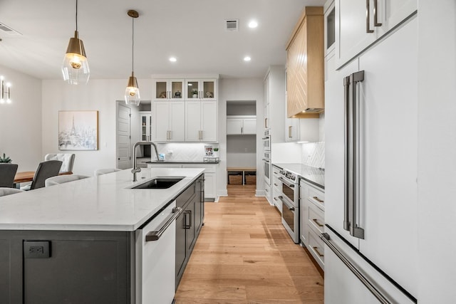 kitchen with dishwasher, white cabinetry, sink, high end fridge, and a center island with sink