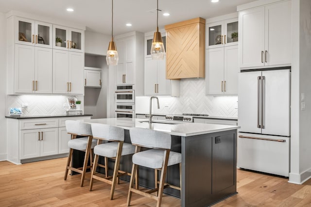 kitchen featuring white cabinetry, white appliances, decorative light fixtures, and an island with sink