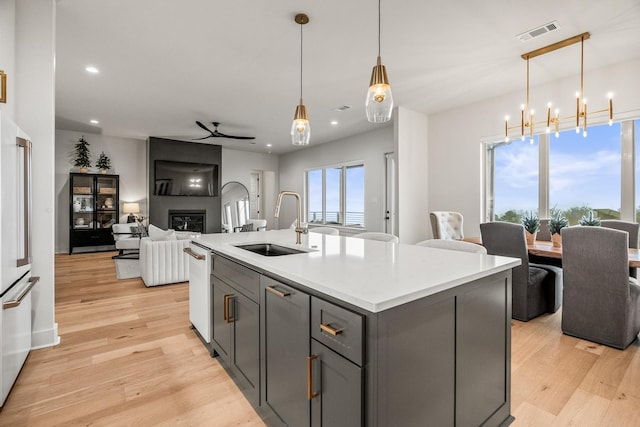 kitchen with sink, light hardwood / wood-style flooring, gray cabinetry, hanging light fixtures, and an island with sink