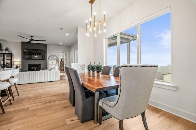 dining room featuring ceiling fan with notable chandelier, a fireplace, and light hardwood / wood-style flooring