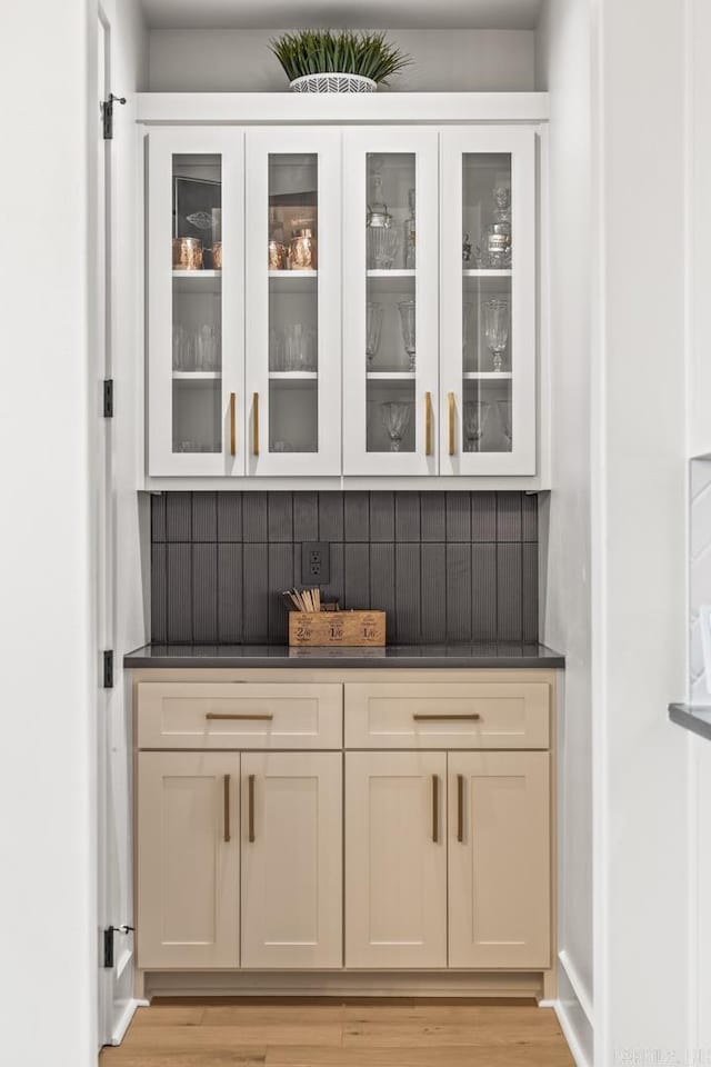 bar featuring cream cabinetry, light wood-type flooring, and backsplash