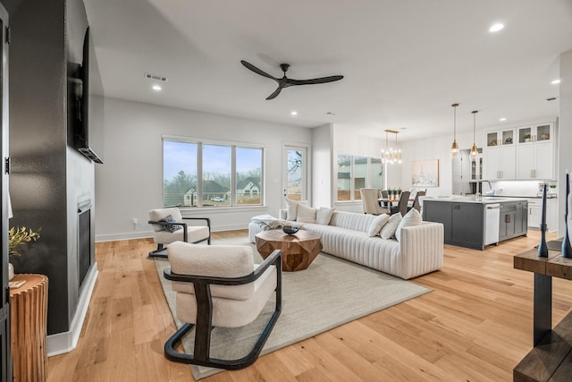 living room with sink, ceiling fan with notable chandelier, a fireplace, and light hardwood / wood-style floors