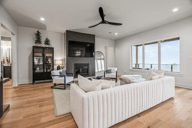 living room with ceiling fan, a fireplace, and light hardwood / wood-style flooring