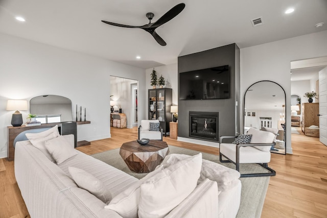 living room with ceiling fan, a large fireplace, and light hardwood / wood-style floors