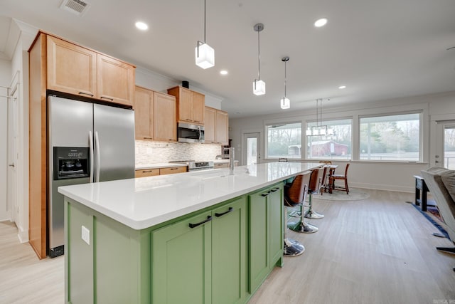 kitchen featuring green cabinetry, appliances with stainless steel finishes, light brown cabinetry, and a kitchen island with sink