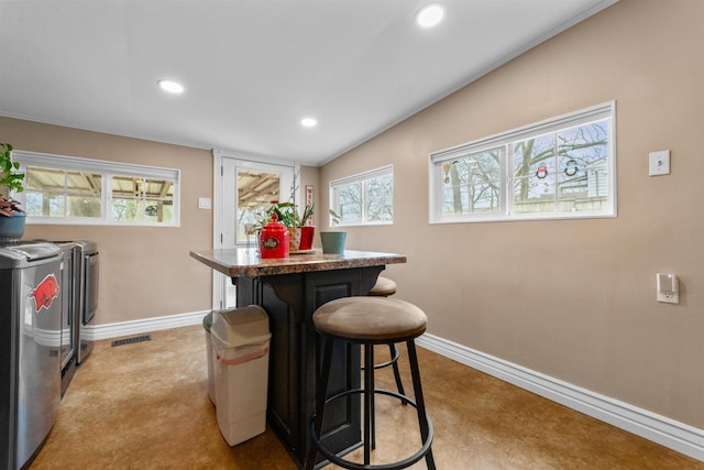 interior space with lofted ceiling, a kitchen breakfast bar, washer and dryer, a kitchen island, and light colored carpet