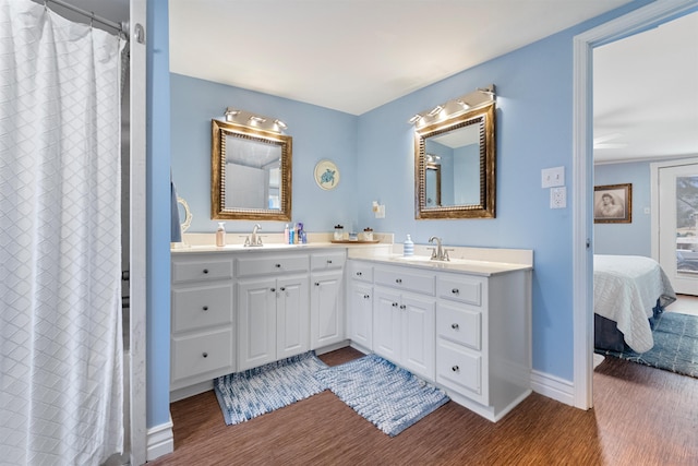 bathroom featuring ensuite bathroom, wood finished floors, a sink, baseboards, and double vanity