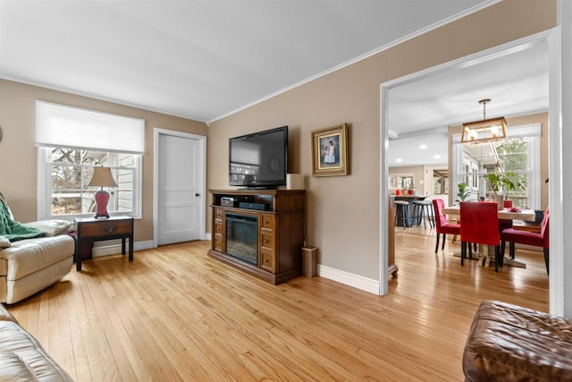 living area with ornamental molding, a glass covered fireplace, light wood-style flooring, and baseboards