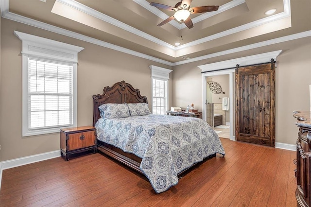 bedroom featuring hardwood / wood-style flooring, a barn door, multiple windows, and a tray ceiling