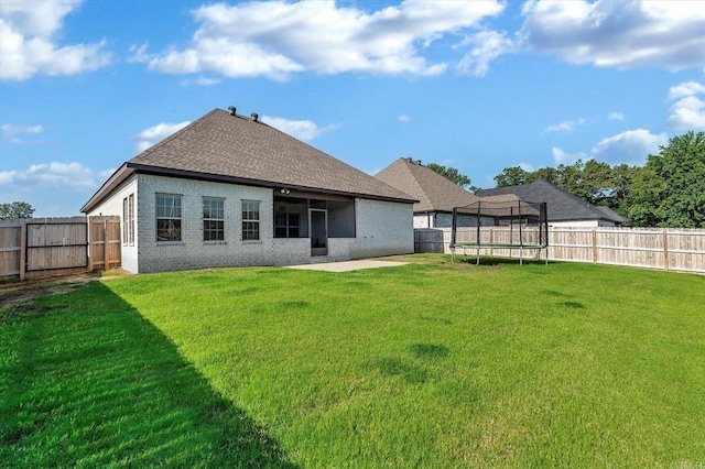 back of property with a yard, a patio, and a trampoline