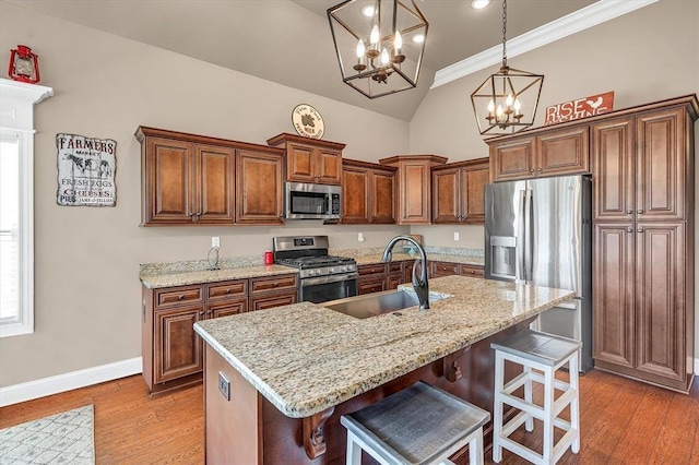 kitchen featuring a breakfast bar, sink, light stone counters, appliances with stainless steel finishes, and a kitchen island with sink