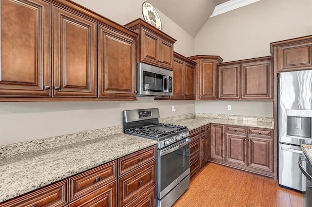 kitchen featuring lofted ceiling, appliances with stainless steel finishes, light stone countertops, and light wood-type flooring