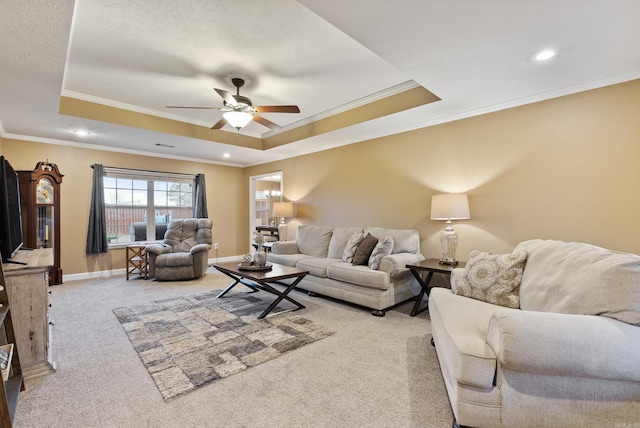 carpeted living room featuring ceiling fan, ornamental molding, and a tray ceiling