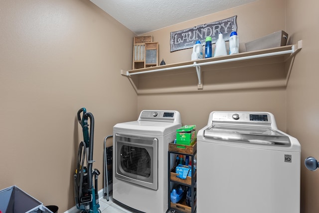 laundry area featuring light tile patterned flooring, washing machine and dryer, and a textured ceiling