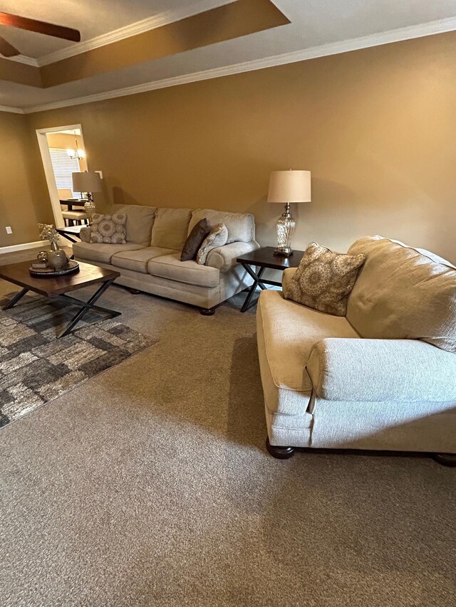 carpeted living room with a tray ceiling, ornamental molding, and ceiling fan