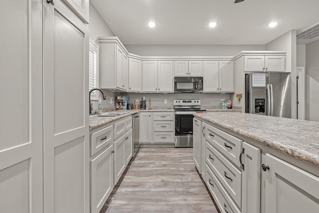 kitchen featuring sink, light hardwood / wood-style flooring, appliances with stainless steel finishes, white cabinetry, and light stone countertops