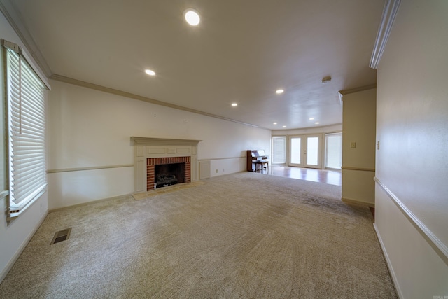 unfurnished living room with crown molding, carpet flooring, a brick fireplace, and french doors