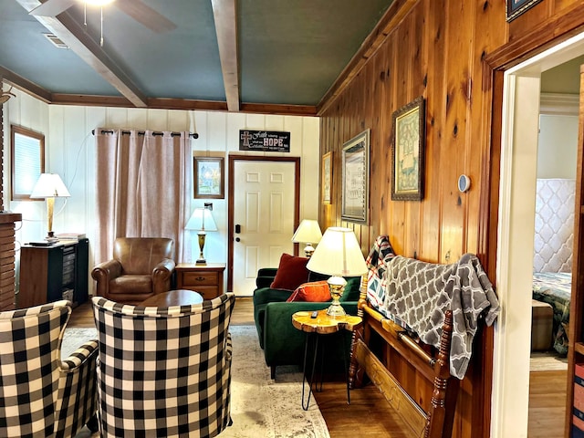sitting room with beam ceiling, ceiling fan, light hardwood / wood-style floors, and wood walls