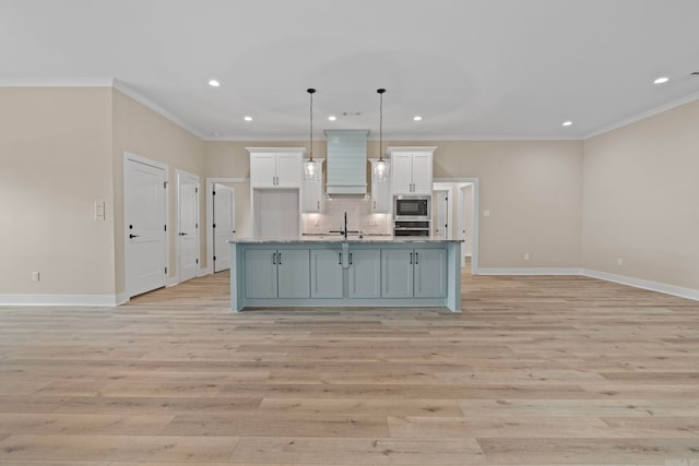 kitchen featuring light hardwood / wood-style flooring, hanging light fixtures, an island with sink, white cabinets, and built in microwave