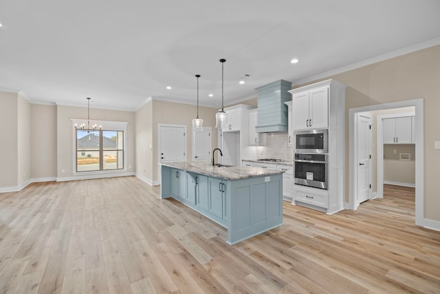 kitchen with a kitchen island with sink, hanging light fixtures, white cabinets, and appliances with stainless steel finishes