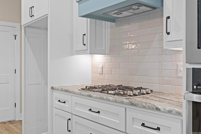 kitchen with premium range hood, light stone counters, stainless steel gas cooktop, white cabinets, and decorative backsplash